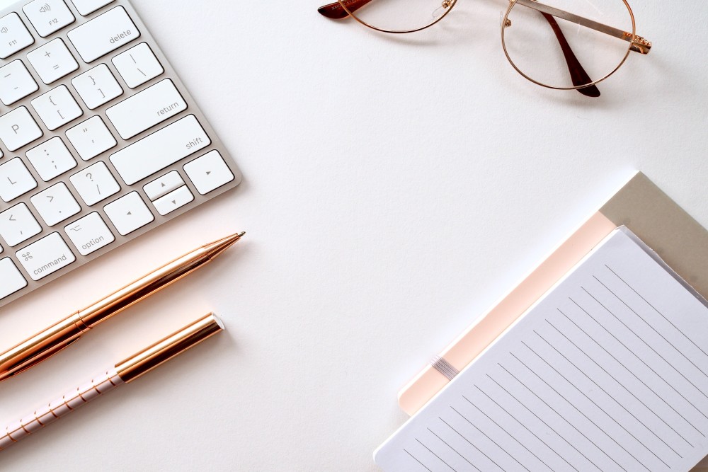 apple keyboard glasses and notebook on white table